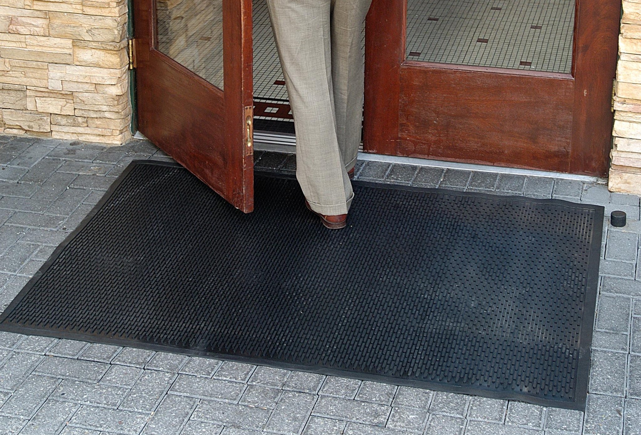 A person walking through a door and stepping on a scraper mat.
