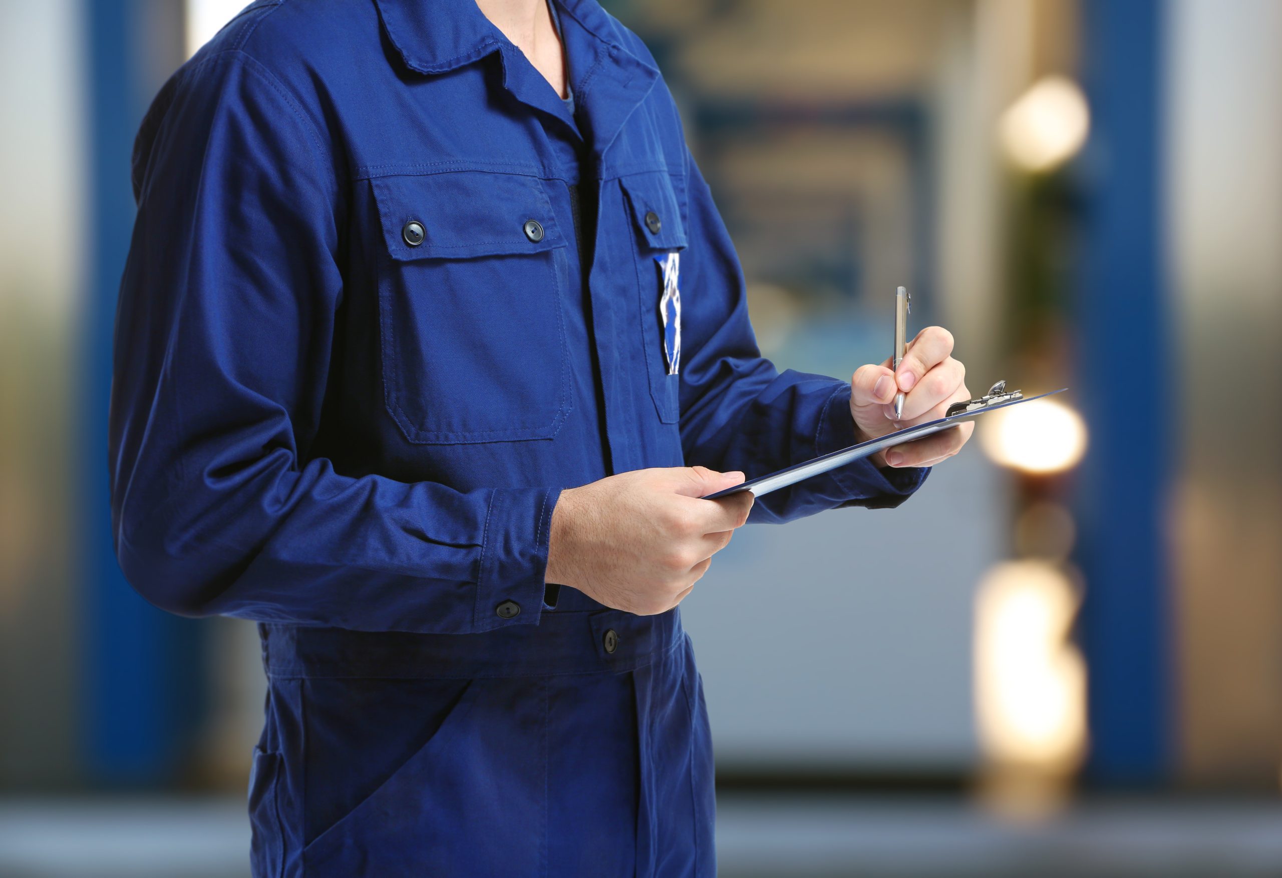 Mechanic in uniform with a clipboard and pen on gas station blurred background