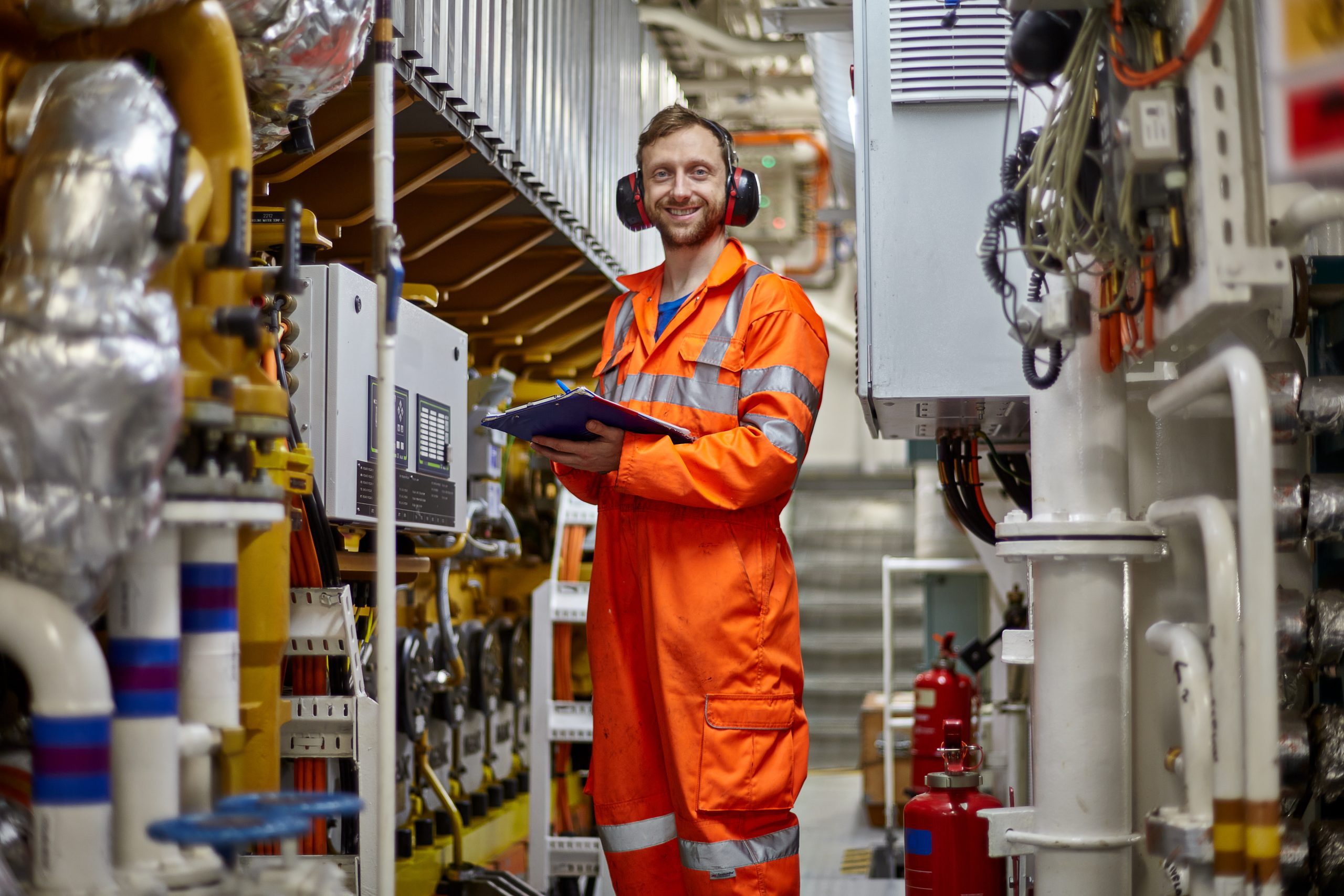 Marine engineer in orange coverall  doing check list on main engine in engine room.