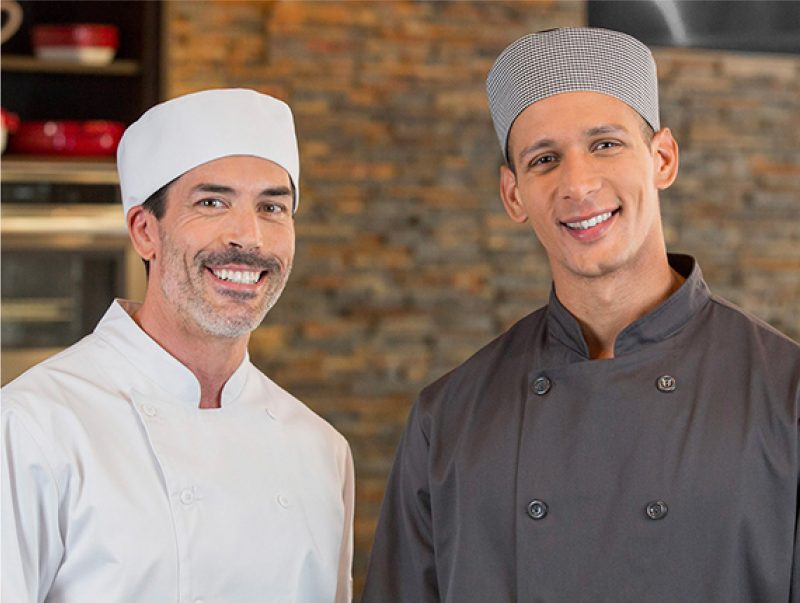 Two chefs smiling wearing pill box caps and chef coats